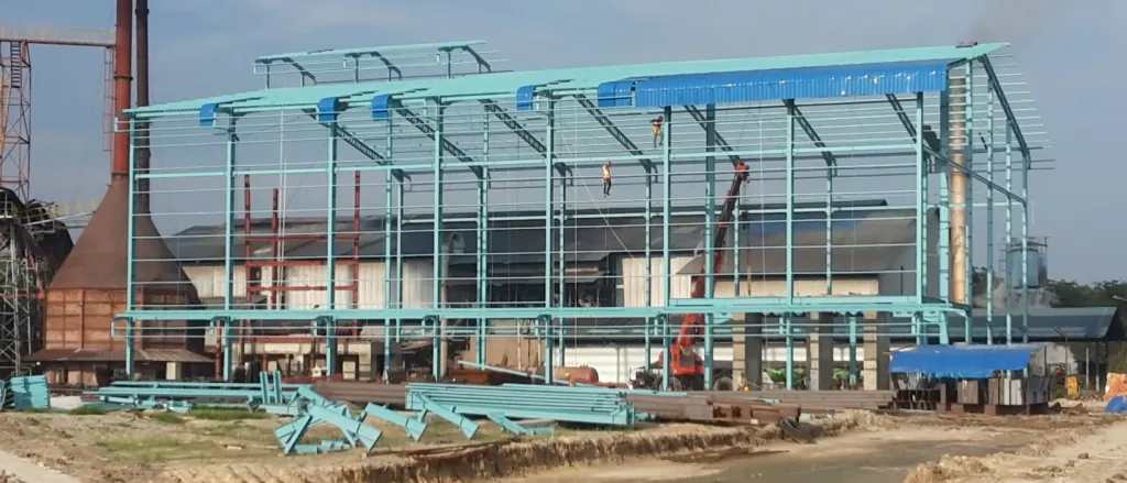 Steel frame of a plant under construction, with smokestacks behind it